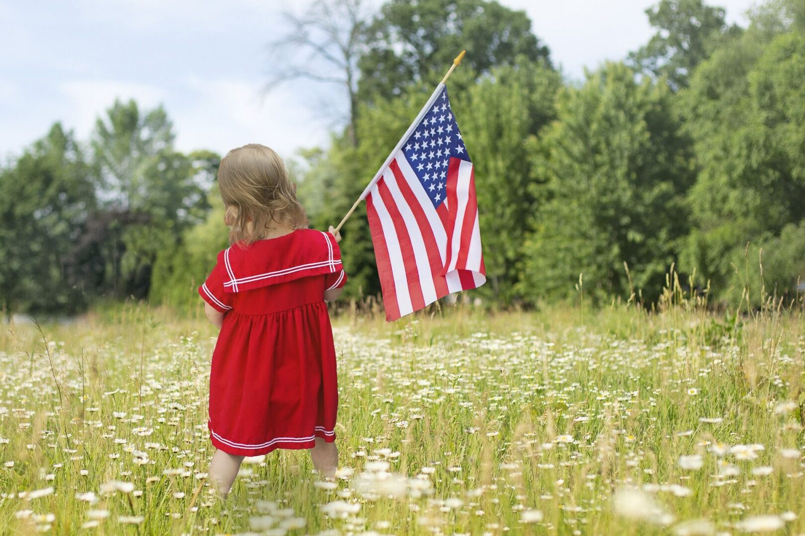 A little girl holding an american flag in the grass.